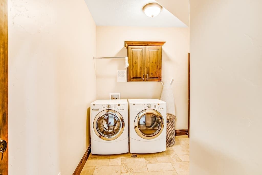 A laundry room with two front-loading washing machines, a wooden cabinet above, and a towel rack.