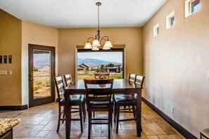 A dining area with a table and chairs, a chandelier, and a view of a desert landscape through a door. - Lovely 4BR Mountainview Zion National Park (Hurricane)