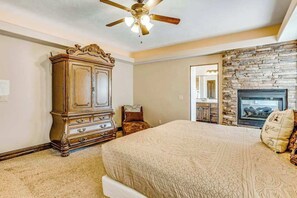 A bedroom with a large bed, a wooden dresser, a stone fireplace, and a ceiling fan. - Lovely 4BR Mountainview Zion National Park (Hurricane)