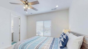 Ein Schlafzimmer mit Bett, Deckenventilator, Fenster mit Jalousien und einer Tür.