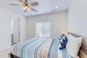 Ein Schlafzimmer mit Bett, Deckenventilator, Fenster mit Jalousien und einer Tür.