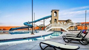 Ein Schwimmbad mit Wasserrutsche, Liegestühlen und einem Gebäude mit Balkon.