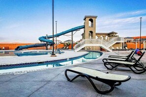Ein Schwimmbad mit Wasserrutsche, Liegestühlen und einem Gebäude mit Balkon.
