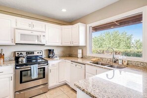 A kitchen with white cabinets, a stainless steel oven, a microwave, a dishwasher, and a window with a view of greenery. - Sunny 2BR Mountainview Zion National Park (St. George)