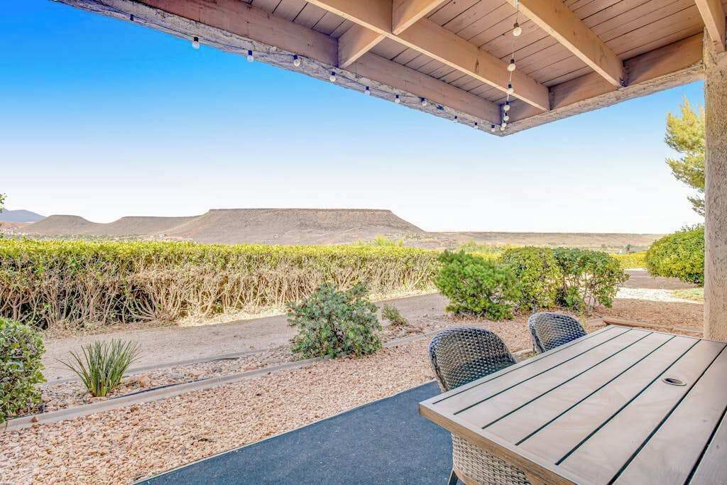 Eine Terrasse im Freien mit Tisch und Stühlen, umgeben von einem angelegten Garten und Blick auf ferne Hügel.