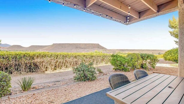 An outdoor patio with a table and chairs, surrounded by a landscaped garden and a view of distant hills. - Sunny 2BR Mountainview Zion National Park (St. George)
