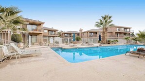 Un edificio residencial con piscina, palmeras y una valla blanca.