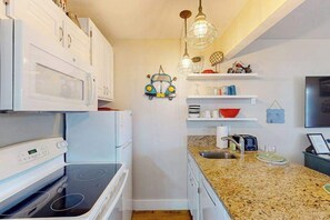 A compact kitchen with white cabinetry, a granite countertop, a built-in microwave, and a gas stove. - 1 BR condo withshared pools, sports courts (Saint George)