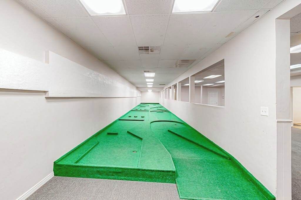A hallway with a green carpeted area, white walls, and ceiling lights.