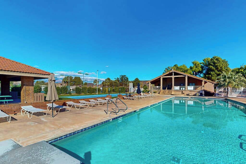 A swimming pool with lounge chairs and umbrellas, a covered seating area, and a clear blue sky.
