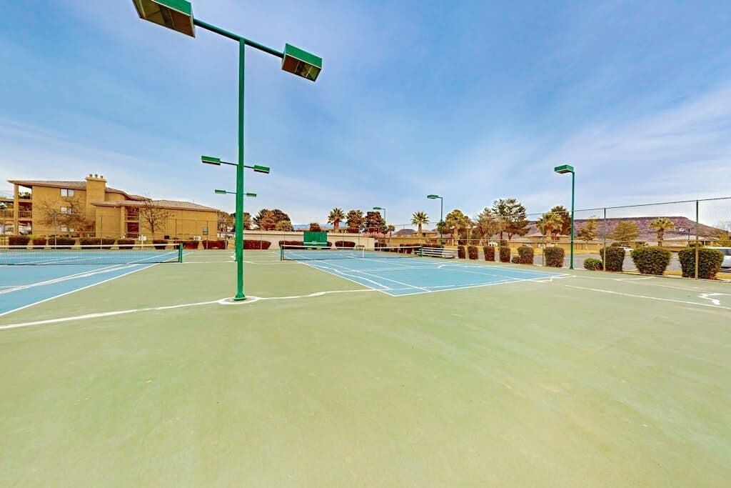 An outdoor tennis court with multiple courts, surrounded by buildings and trees.