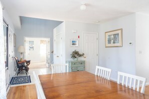 A dining room with a wooden table and white chairs, a blue wall, and a door leading to another room.