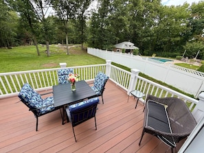 A deck with a table and chairs, surrounded by a white fence, overlooking a backyard with a pool.