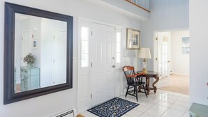 A hallway with white doors, a large mirror, a wooden chair, a small table with a lamp, and a patterned rug.