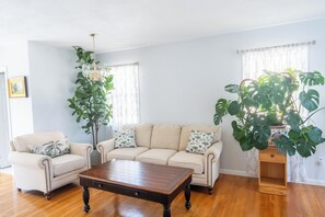 A living room with a sofa, two armchairs, a coffee table, a chandelier, and large potted plants.