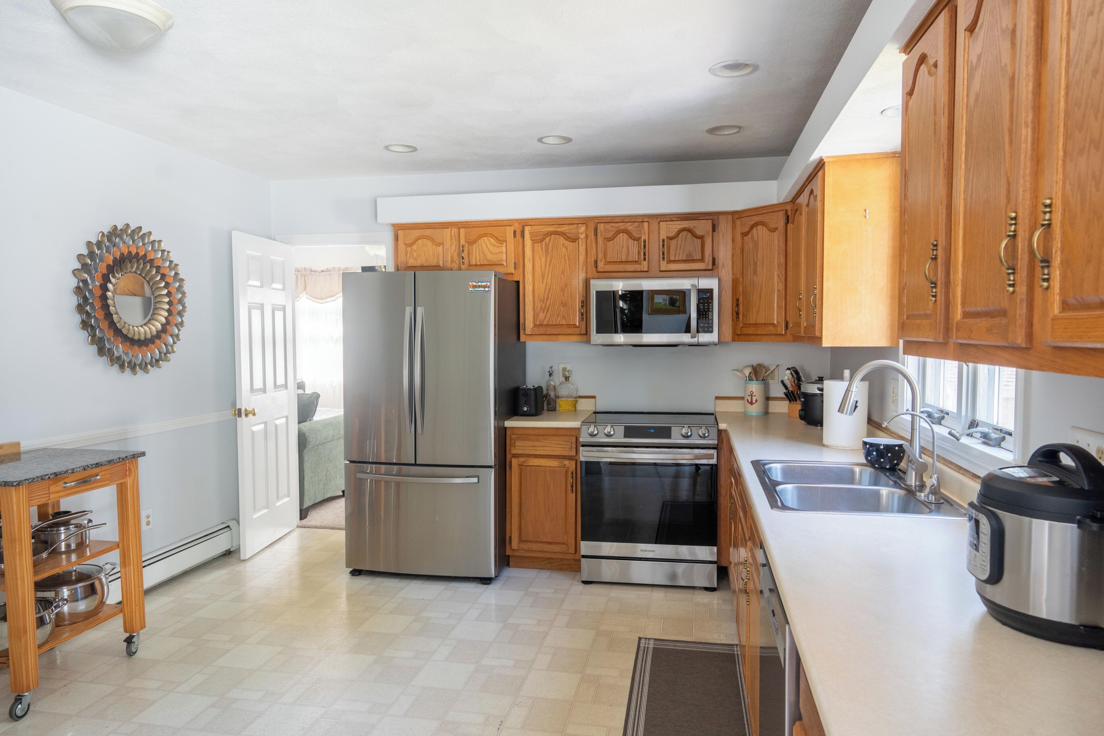 A modern kitchen with stainless steel appliances, wooden cabinets, and a large window providing natural light.