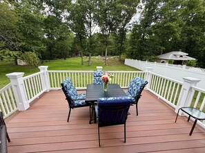 A deck with a table and chairs, surrounded by a white fence, overlooking a grassy yard.