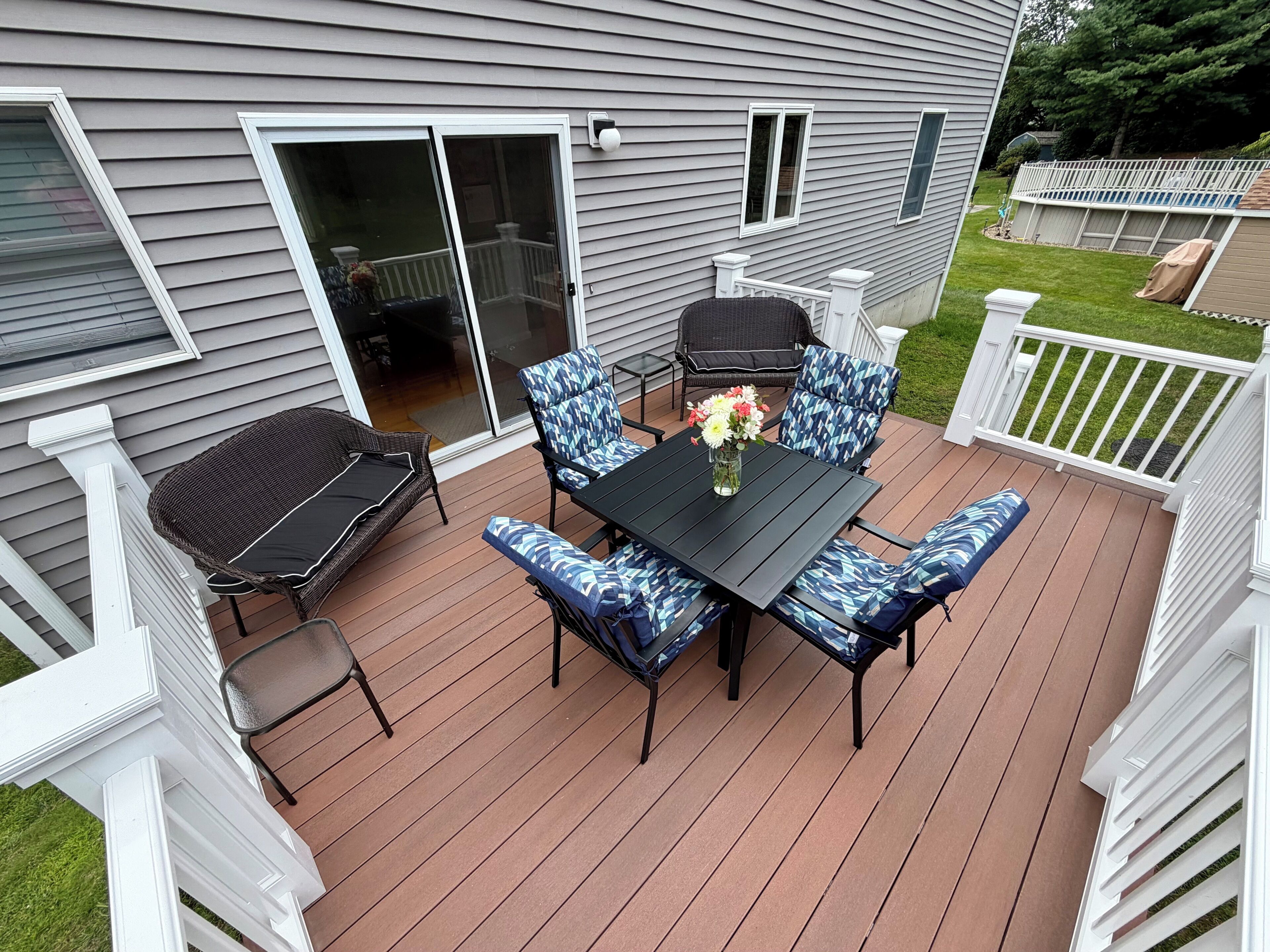 A deck with a table and chairs, a sliding glass door, and a white fence.