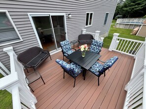 A deck with a table and chairs, a sliding glass door, and a white fence.