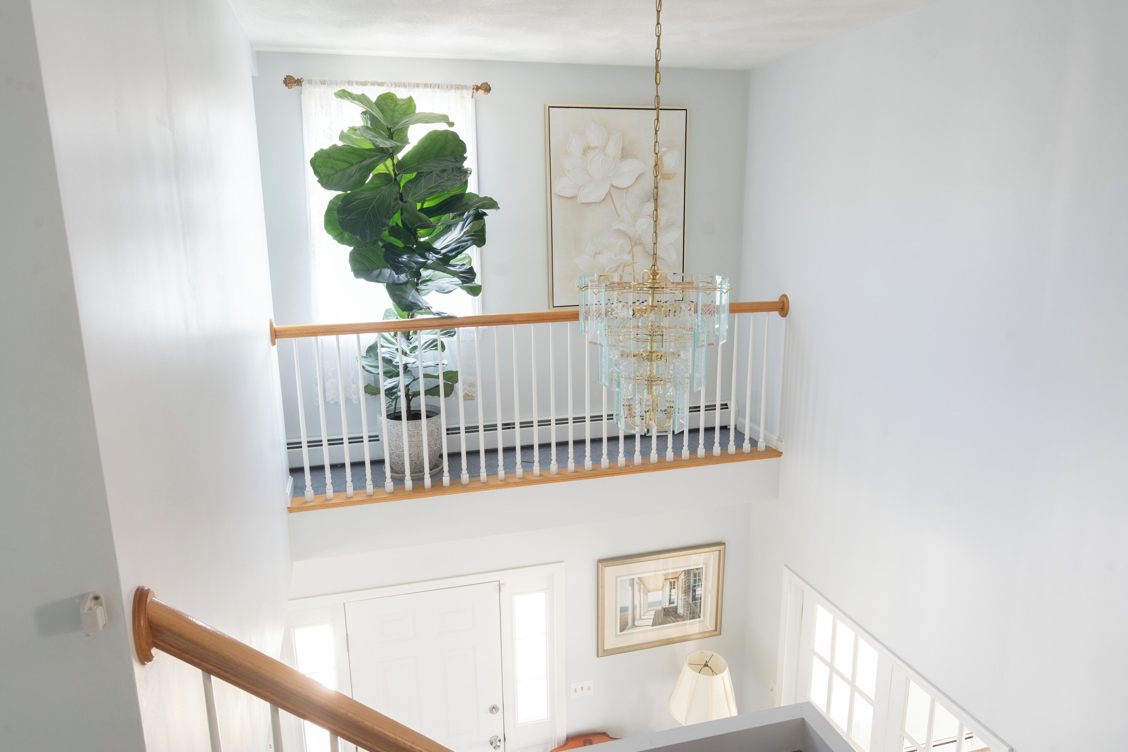 A staircase with a wooden handrail, a potted plant, a chandelier, and a framed picture on the wall.