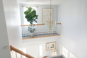 A staircase with a wooden handrail, a potted plant, a chandelier, and a framed picture on the wall.