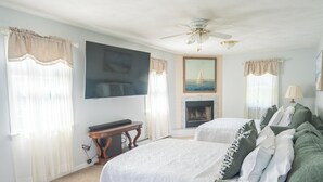 A hotel room with two beds, a flat-screen TV, a fireplace, and a ceiling fan.