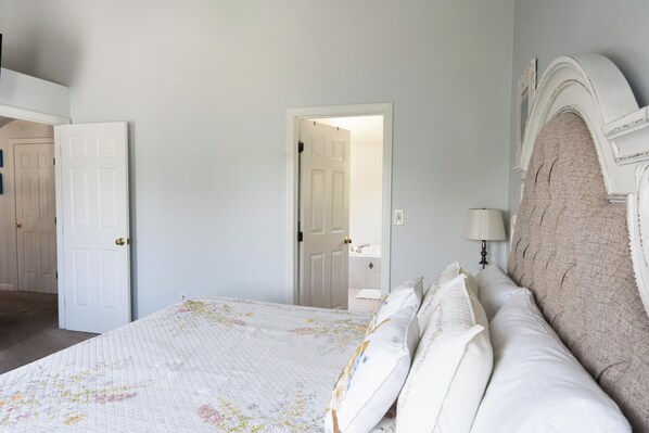 A bedroom with a large bed, a nightstand, a lamp, and a door leading to a bathroom.