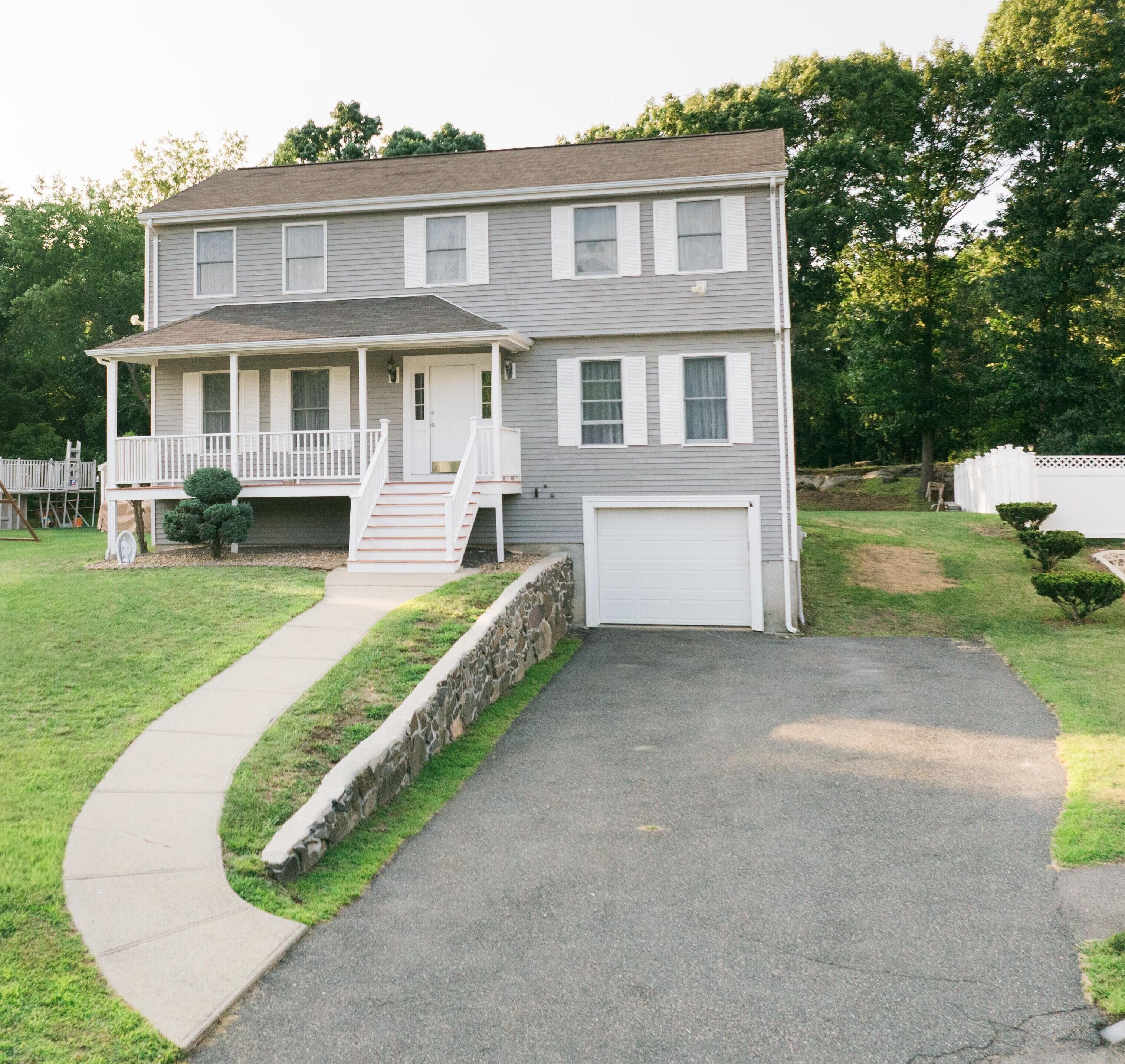 A two-story house with a front porch, a garage, and a stone retaining wall.