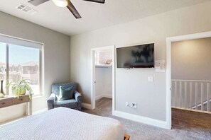 Un dormitorio con cama, una silla, un televisor y vistas de la ciudad a través de un amplio ventanal.