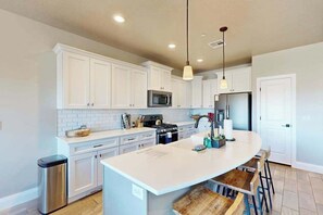 A kitchen with white cabinets, a central island with stools, stainless steel appliances, and pendant lighting. - Townhouse with resort amenities, private hot tub (Hurricane)