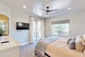 A bedroom with a bed, a television mounted on the wall, a ceiling fan, and a window with curtains. - Townhouse with resort amenities, private hot tub (Hurricane)