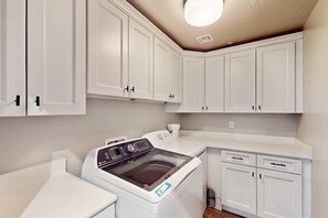 A laundry room with a front-loading washing machine, a dryer, and white cabinetry. - Townhouse with resort amenities, private hot tub (Hurricane)
