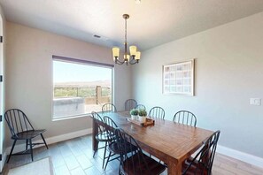 A dining area with a wooden table, six chairs, a chandelier, and a large window with a view. - Townhouse with resort amenities, private hot tub (Hurricane)