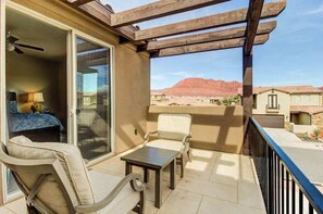 A balcony with a view of red rock formations, a sliding glass door leading to a room with a bed and a lamp, and a small table. - 3BR Mountainview Paradise Village - Pool (Santa Clara)