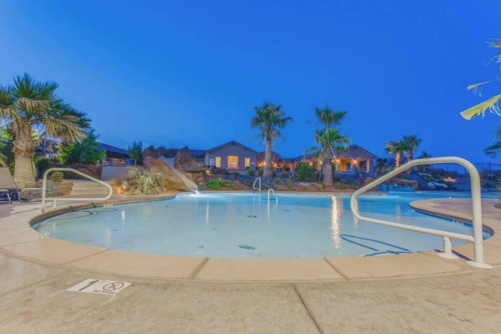 A swimming pool with a no diving sign, surrounded by palm trees and houses in the background.