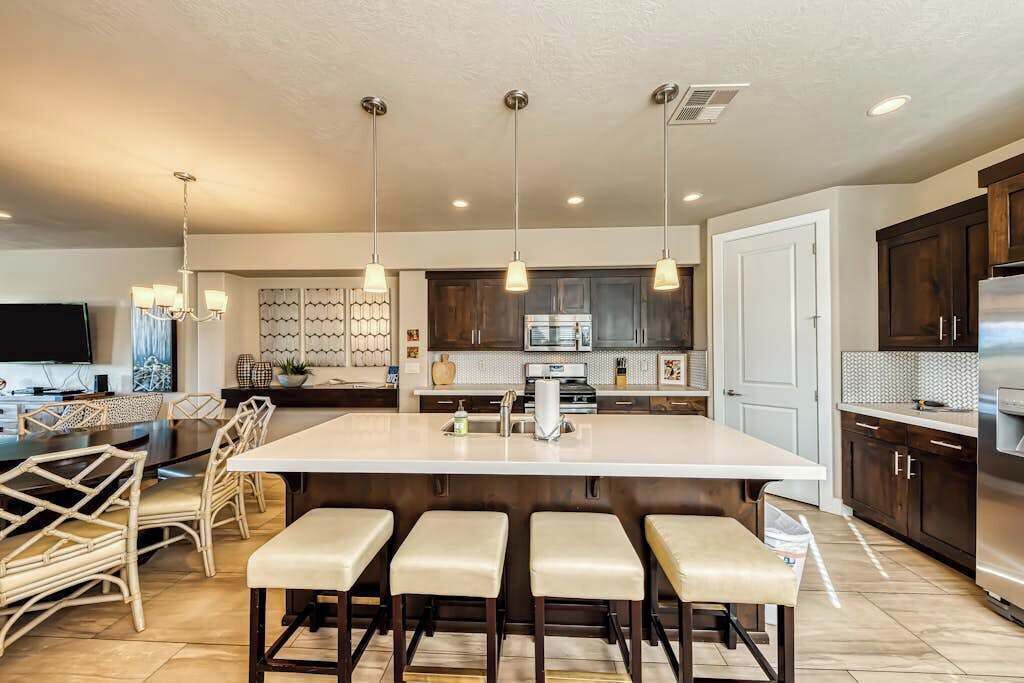 A modern kitchen with a central island, bar stools, pendant lighting, and stainless steel appliances.