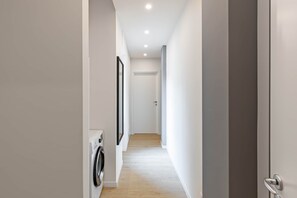 A narrow hallway with a washing machine on the left, a door at the end, and a light-colored floor. - Blue Two-Room Apartment with a Terrace, 5 Minutes from the Station (Bergamo)