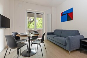 Ein modernes Wohnzimmer mit einem grauen Sofa, einem Esstisch mit Stühlen und einem an der Wand befestigten Fernseher.