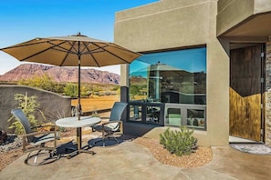 An outdoor patio with a table and chairs, a large umbrella, and a view of a mountainous landscape. - Mountain View Studio Near Zion National Park (St. George)
