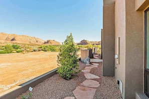 A building with a stone pathway leading to a door, surrounded by a gravel area and sparse vegetation. - Mountain View Studio Near Zion National Park (St. George)