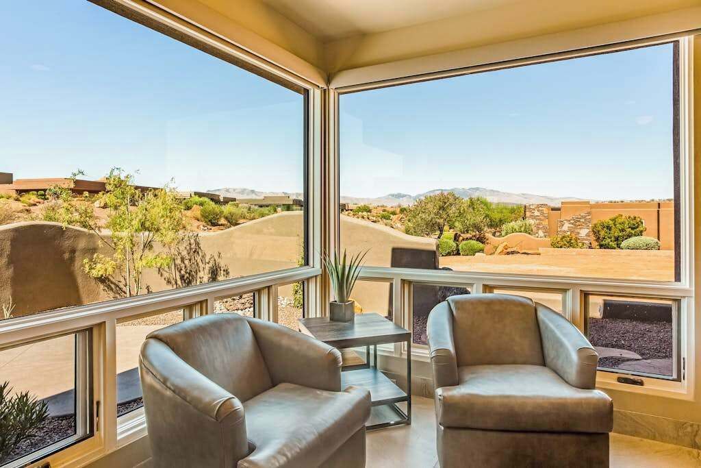 A room with two leather chairs, a small table, and a view of a desert landscape through large windows.