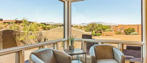 A room with two leather chairs, a small table, and a view of a desert landscape through large windows.