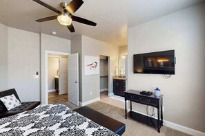 Ein Schlafzimmer mit einem Bett, einem Deckenventilator, einem Fernseher und einem Schreibtisch.