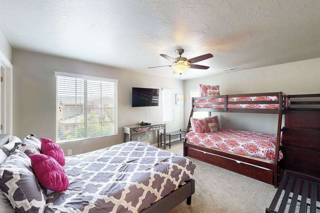 Une chambre à coucher comprenant un lit, un bureau, un lit superposé et un ventilateur de plafond.