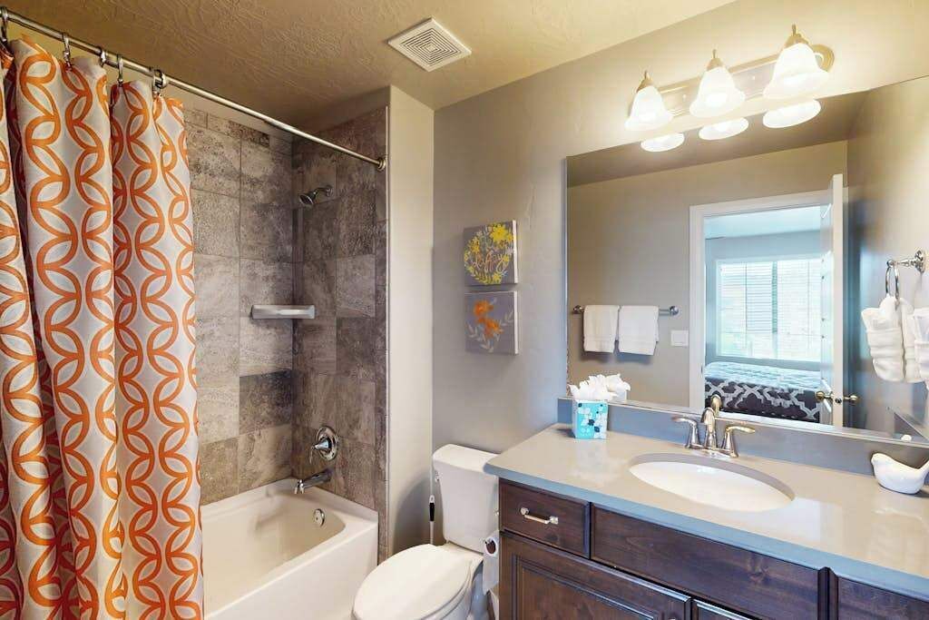A bathroom with a shower, toilet, vanity, and a large mirror.