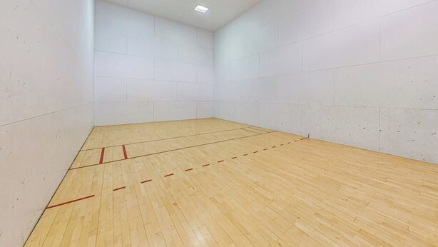 Uma quadra de squash com piso de madeira e paredes brancas.