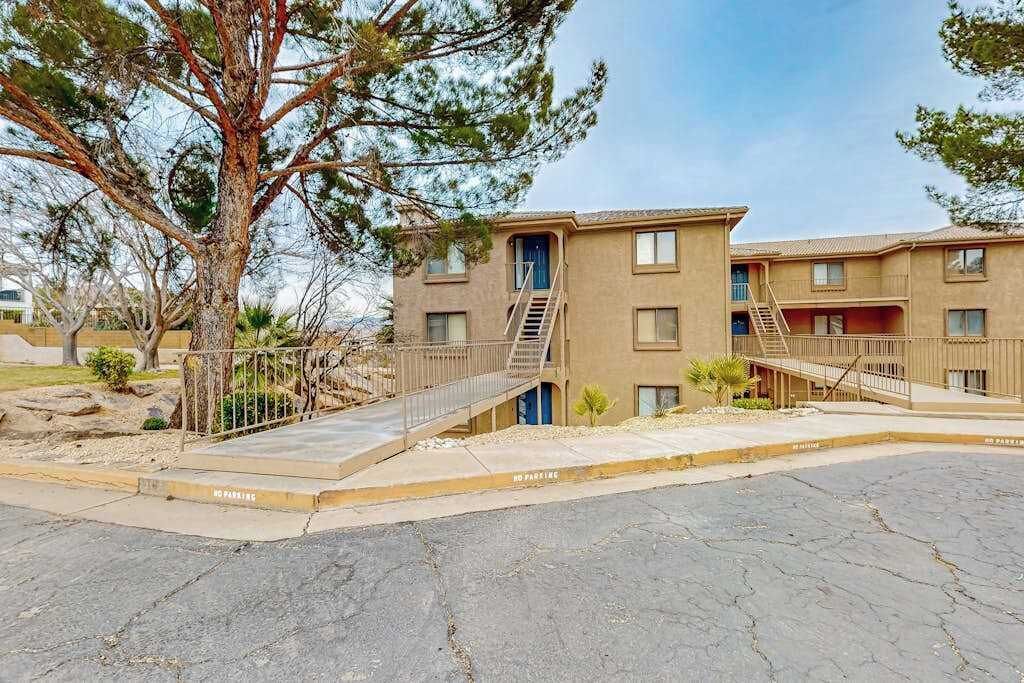 A multi-story residential building with a central staircase, a covered parking area, and a tree in the foreground.
