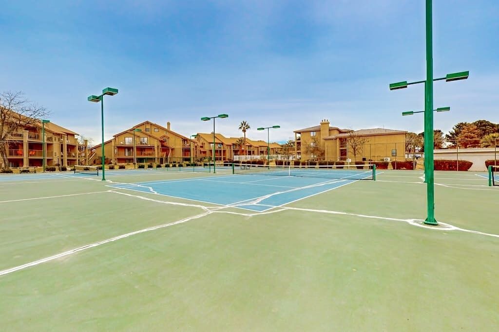 Ein Außen-Tennisplatz mit umliegenden Gebäuden, darunter ein Hotel mit Balkonen.