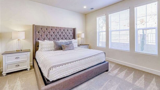 A bedroom with a tufted headboard, two bedside tables with lamps, a large bed with a patterned bedspread, and three windows with blinds. - 5BR townhouse with lazy river pool (Washington)