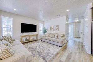 A spacious living room with a large flat-screen TV, a beige sofa set, a marble-patterned rug, and hardwood flooring. - 5BR townhouse with lazy river pool (Washington)